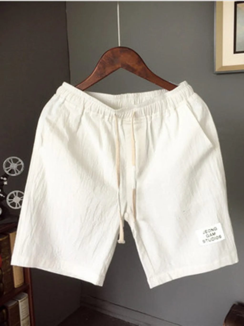 White shorts on a wooden hanger against a gray wall.