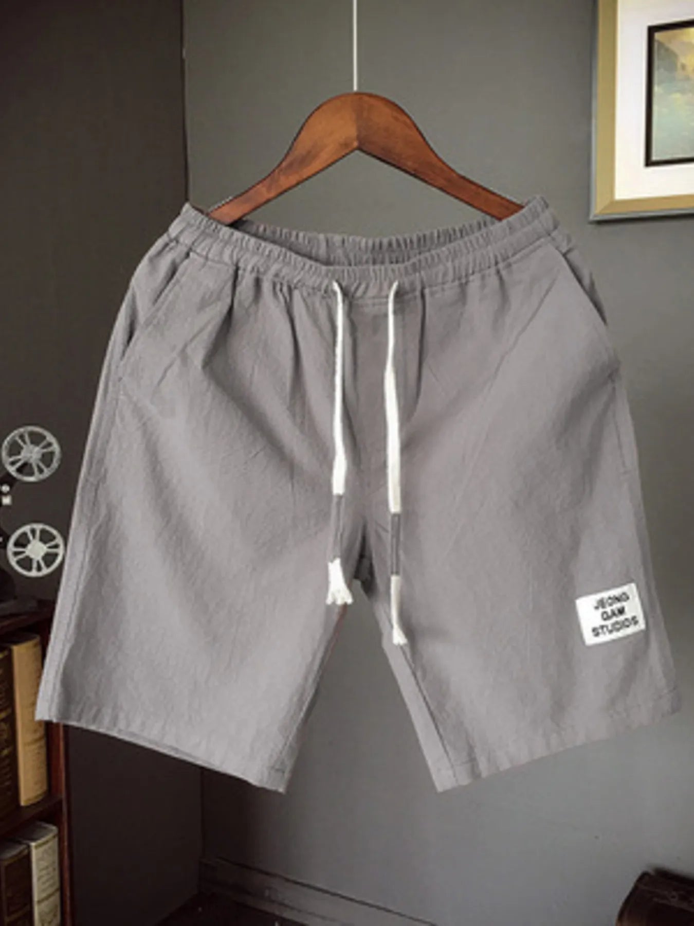 Gray shorts with a drawstring on a hanger against a gray wall.