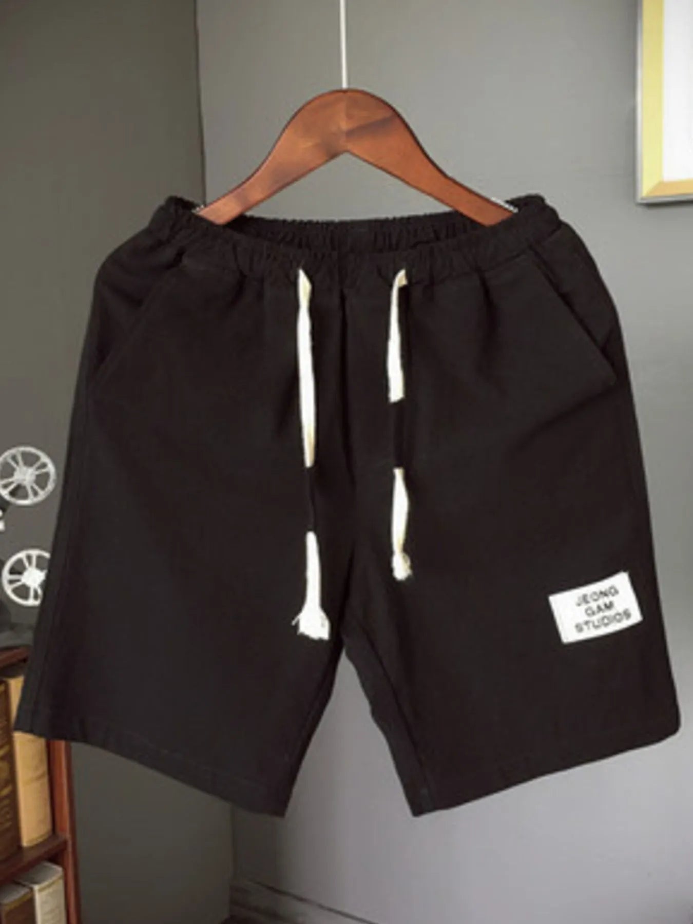 Black shorts with drawstrings on a hanger against a gray wall.