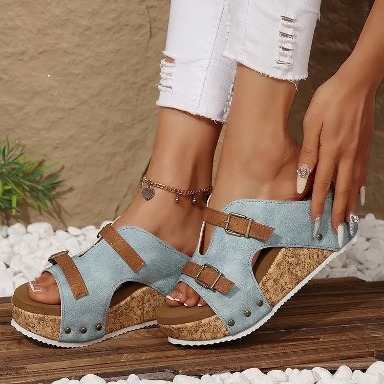 Light blue wedge sandals with brown straps worn by a person on a wooden surface.