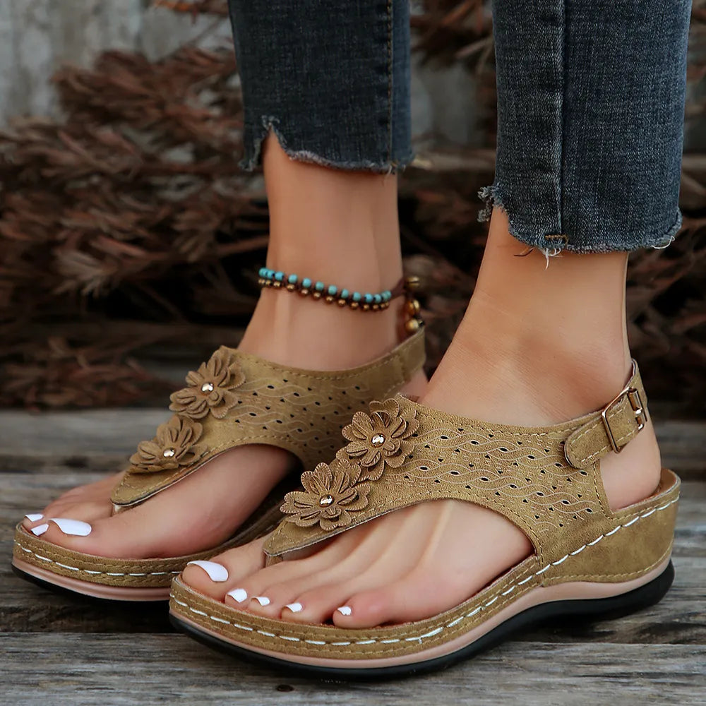 Brown sandals with floral designs worn by a person on a wooden surface.