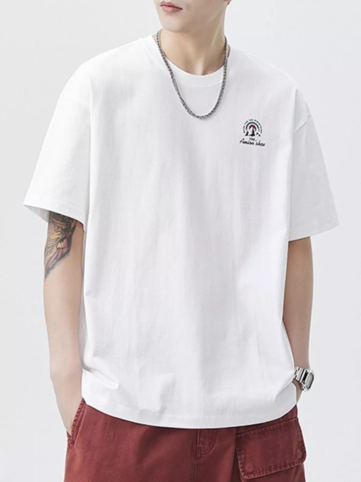 Person wearing a white t-shirt with a logo and red pants on a plain background-blackorvani.com