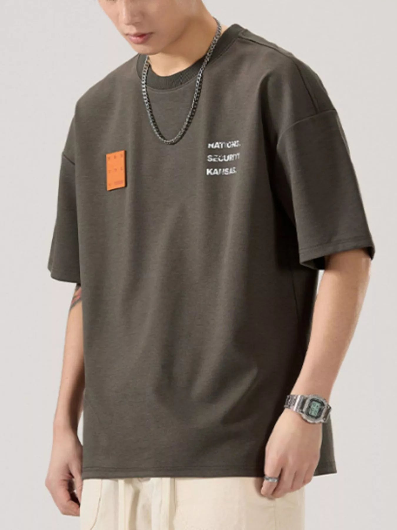 men wearing a dark gray t-shirt with text and a square patch on a light gray background