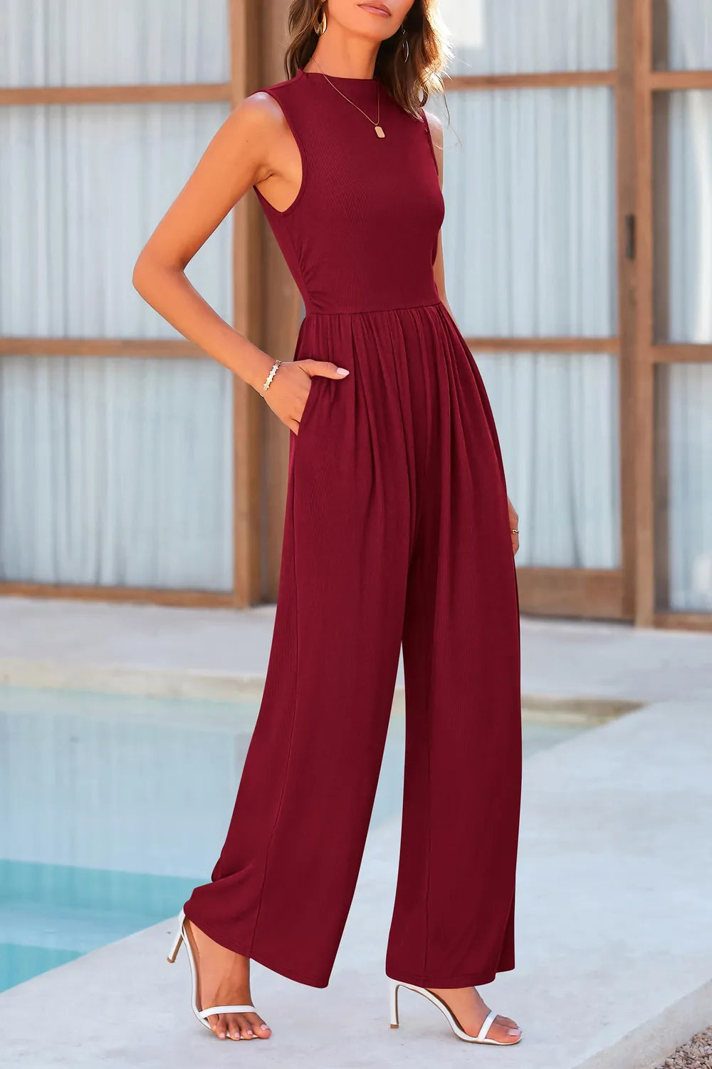 Woman wearing a burgundy jumpsuit by a poolside-blackorvani.com