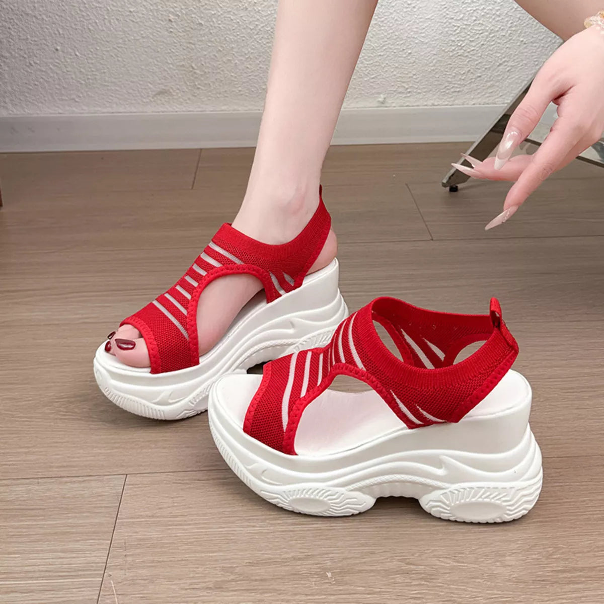 Red platform sandals with white chunky soles, shown on a model's feet and one placed on a wooden floor.