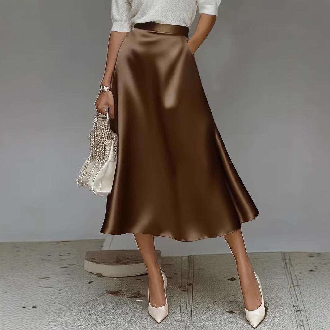 Person wearing a brown satin skirt with a white top and shoes, holding a clutch against a neutral background.
