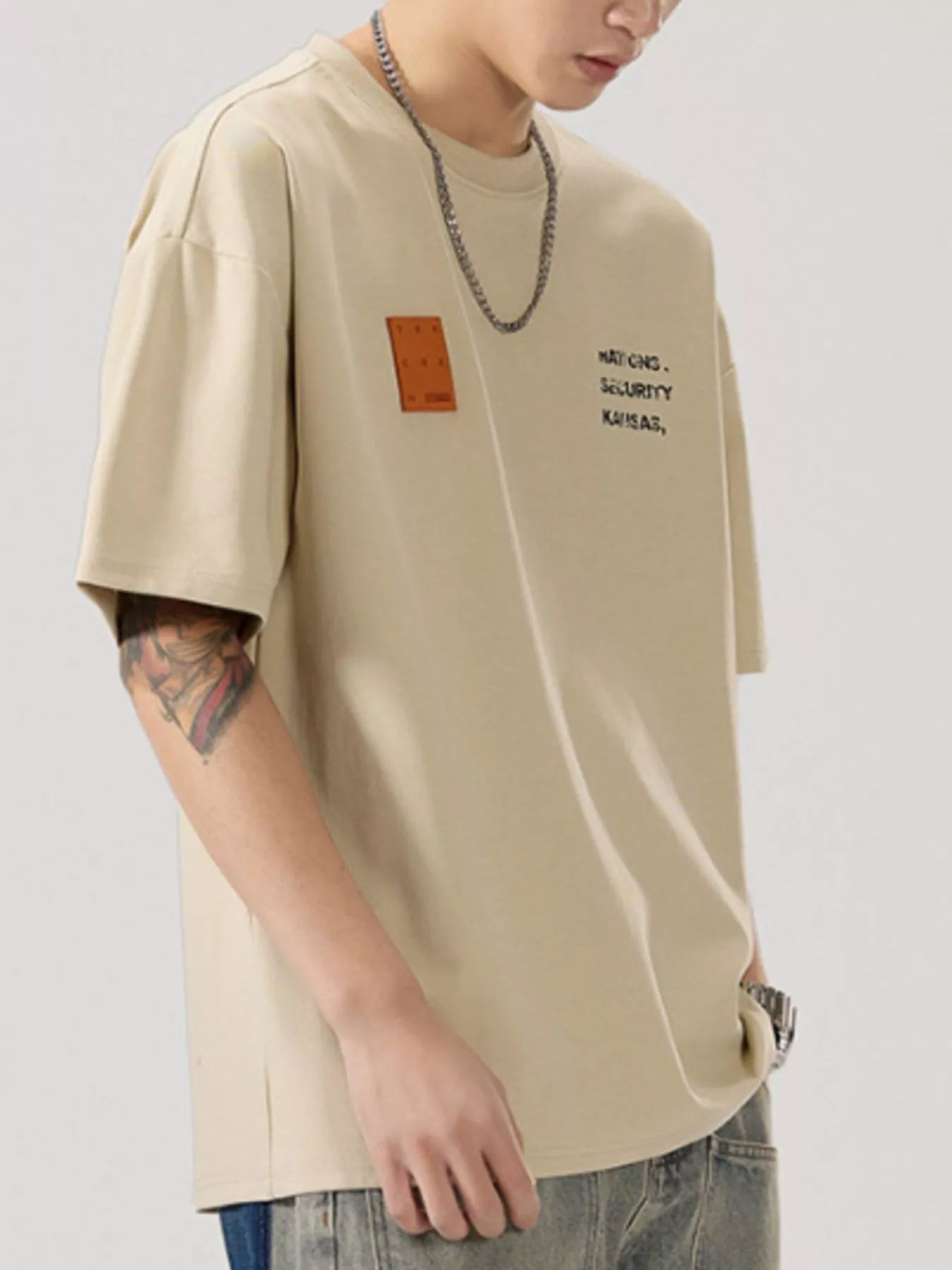 men wearing a beige t-shirt with text and a patch on a plain background