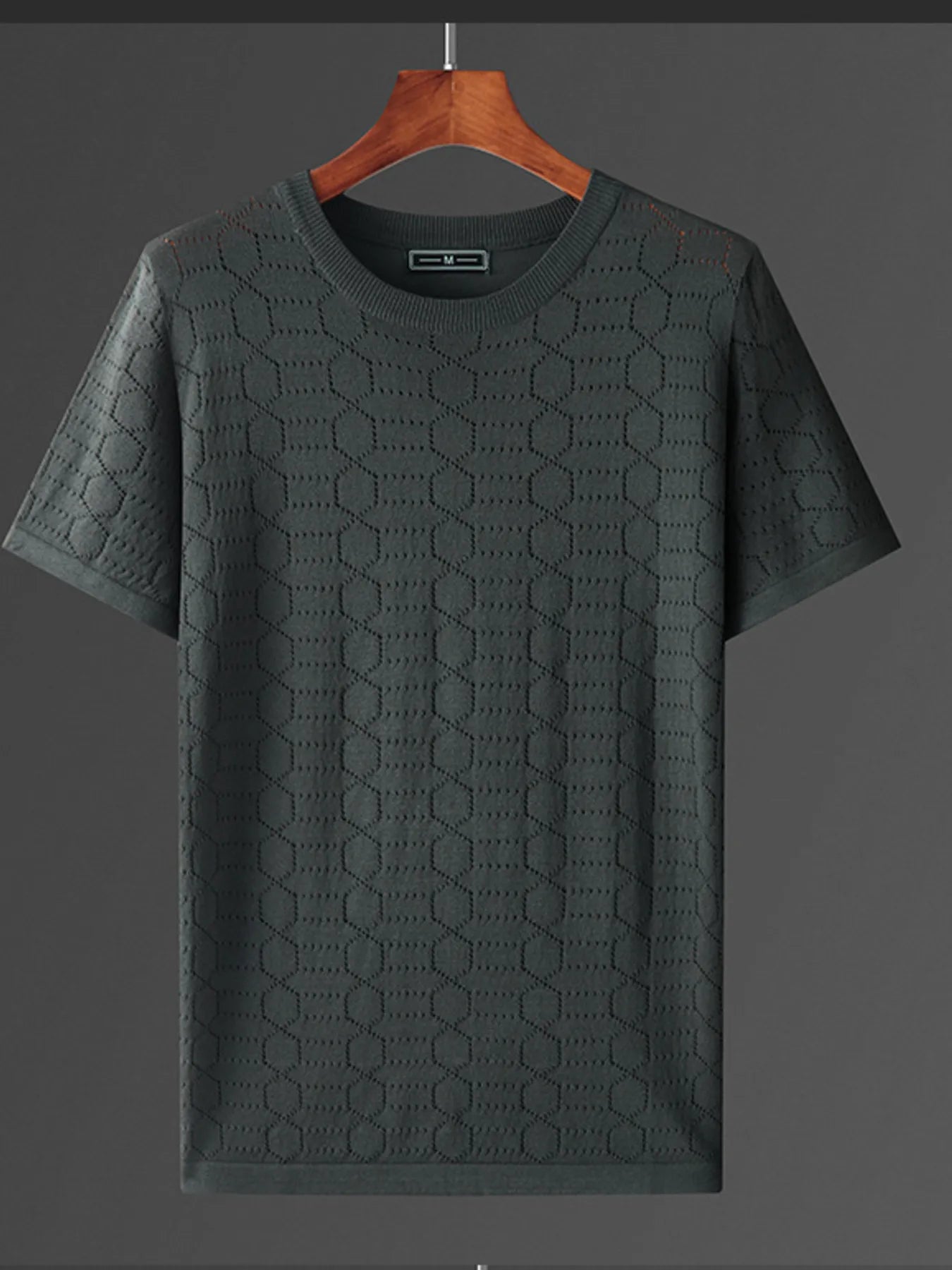 Green textured t-shirt on a wooden hanger against a gray background