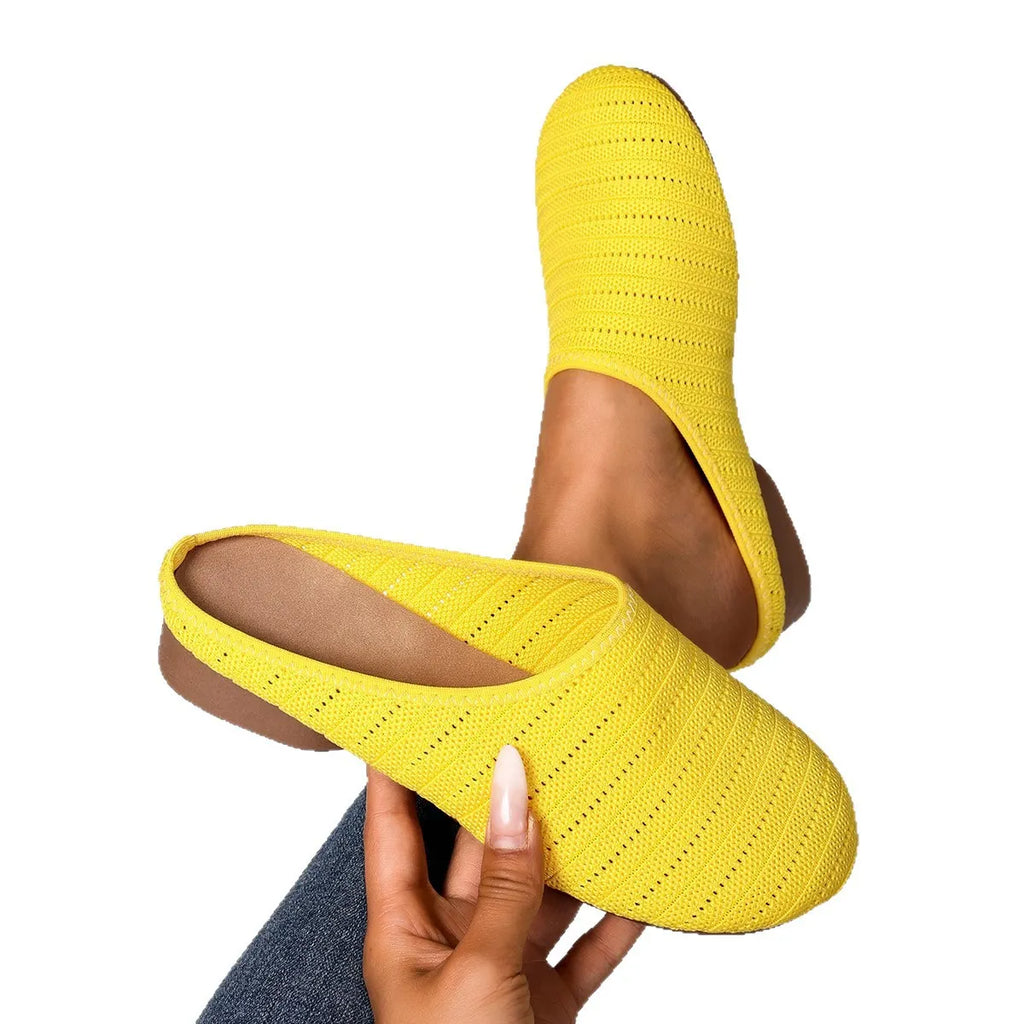 Yellow slippers being held by a hand on a white background