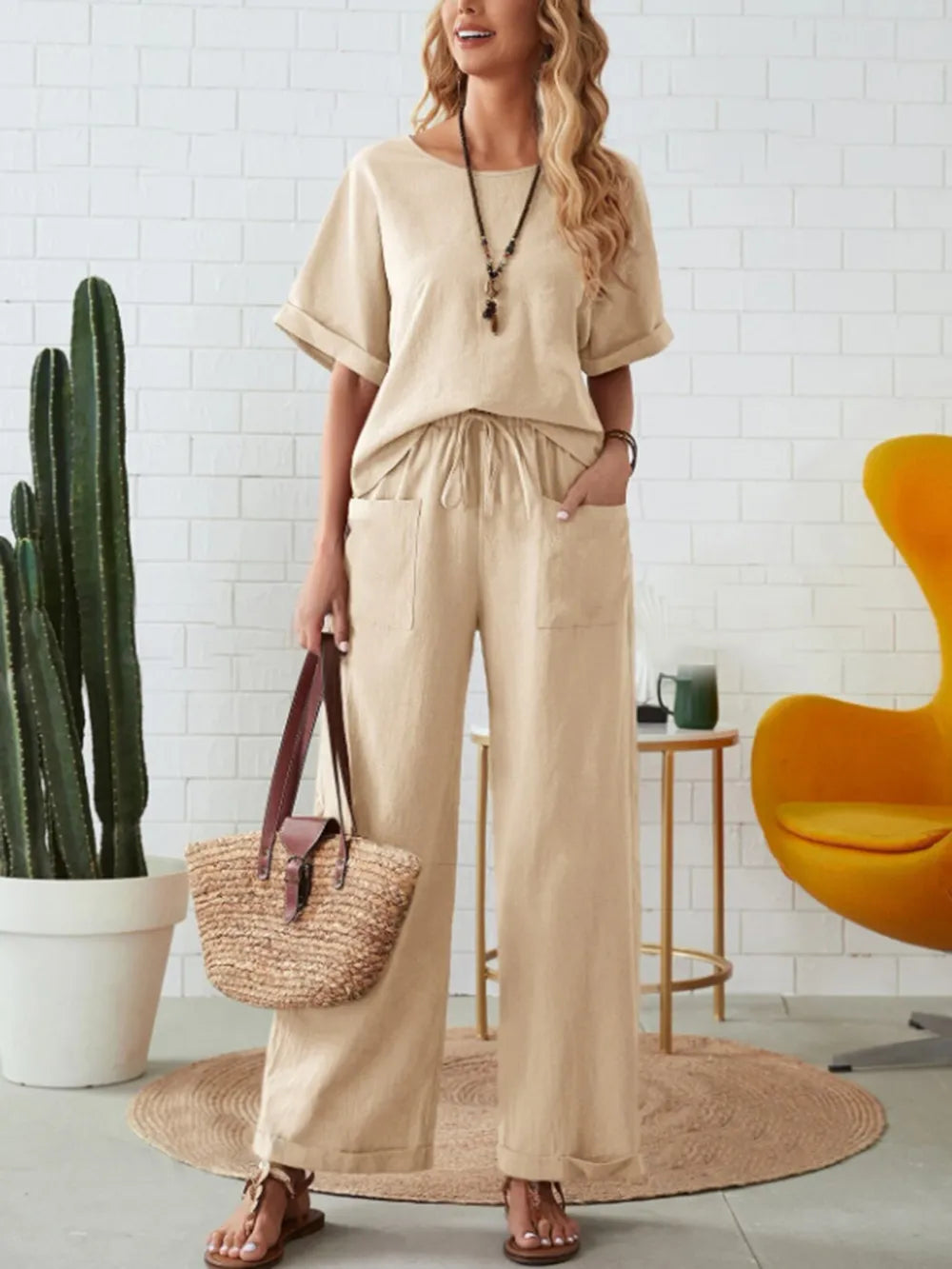 Woman in beige outfit holding a straw bag in a room with a cactus and yellow chair-blackorvani