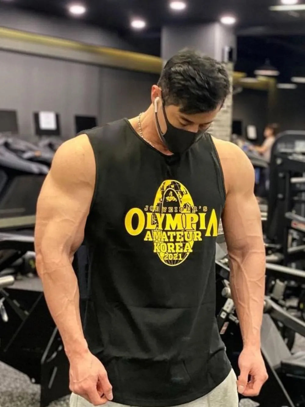 Person wearing a black tank top with '奥林匹亚业余韩国2021' text in a gym setting-blackorvani.com