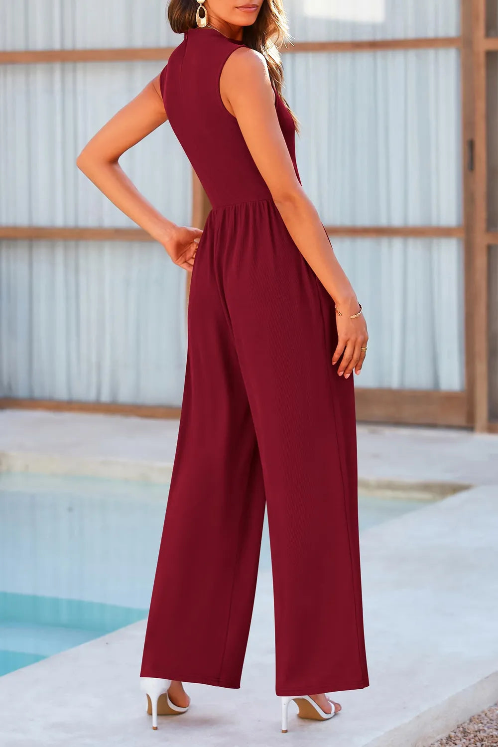 Woman wearing a burgundy jumpsuit by a poolside-blackorvani.com