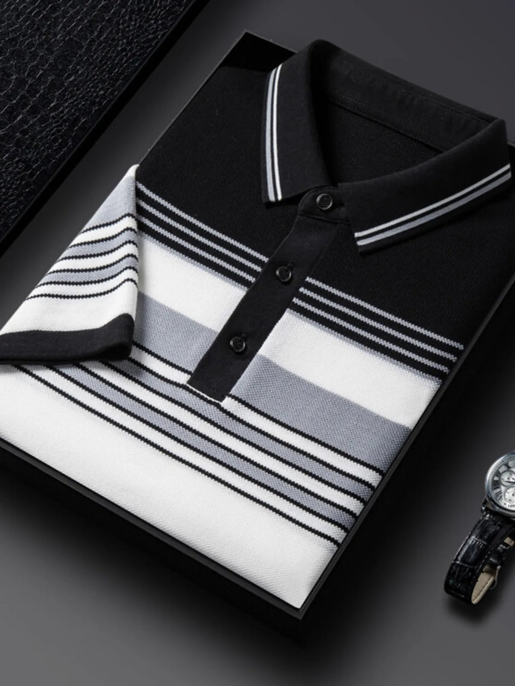 Black and white striped polo shirt on a dark surface with a watch beside it-blackorvani.com