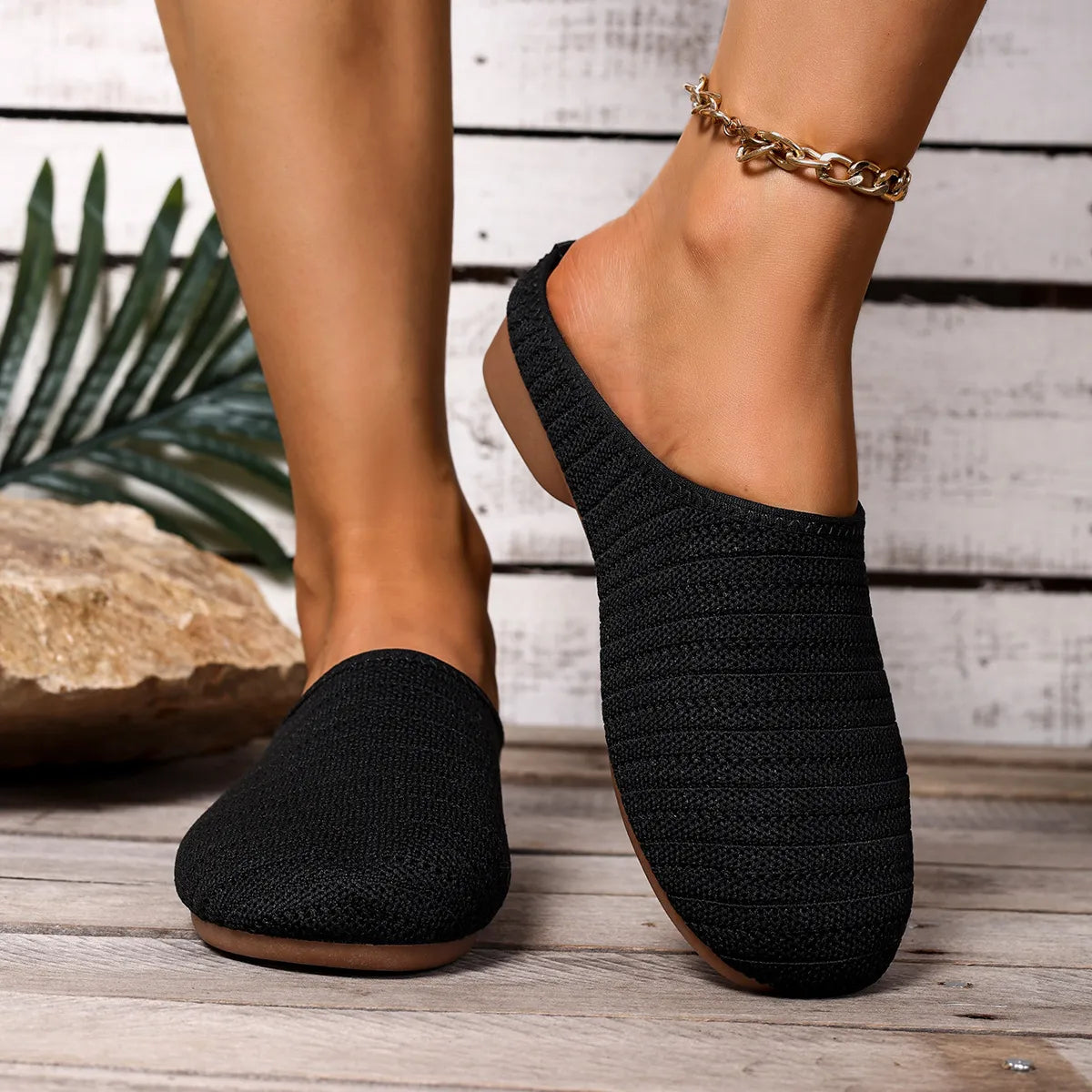 Black knitted slippers worn on a wooden floor with a plant in the background
