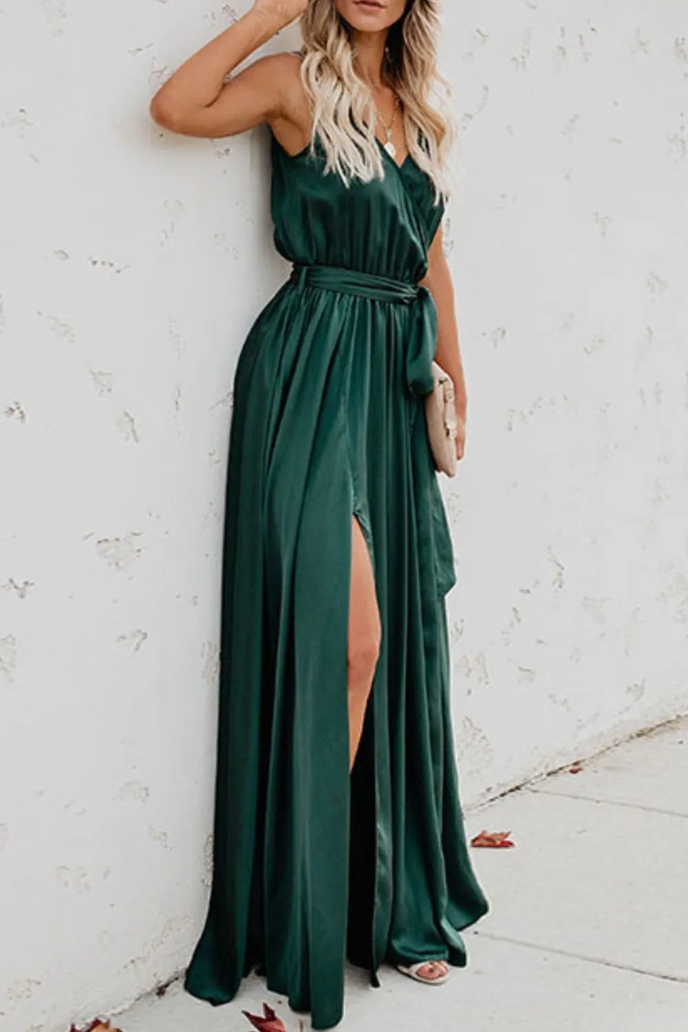 Woman wearing a green dress with a slit, standing against a white wall.