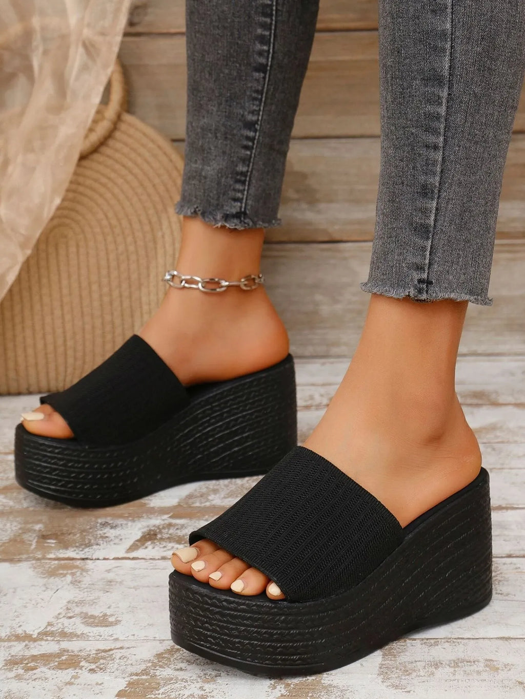 Black wedge sandals worn with gray jeans on a wooden floor.