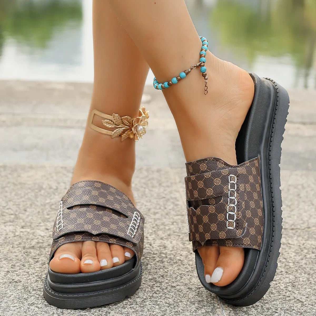 Brown patterned sandals worn on feet with accessories, blurred background