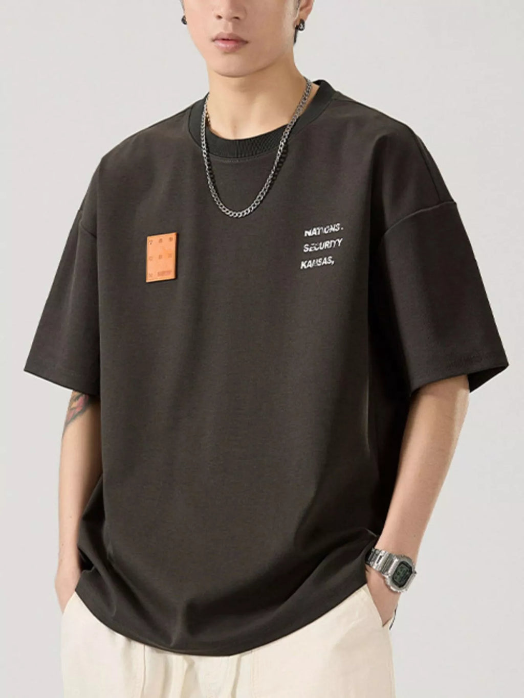 Person wearing a black t-shirt with text and a patch on a plain background