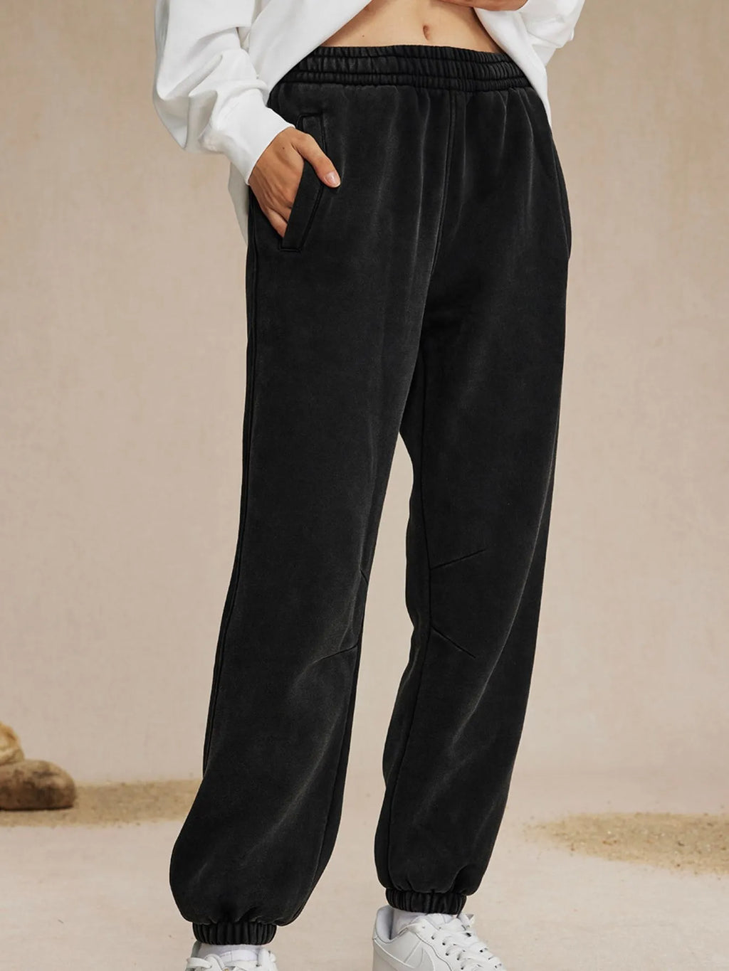 Black sweatpants worn with a white top on a beige background-blackorvani.com
