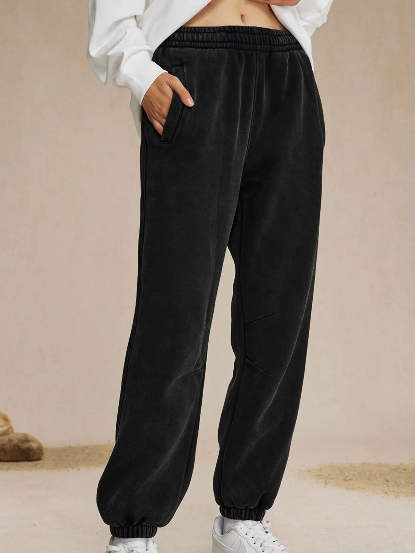 Black sweatpants worn with a white top on a beige background-blackorvani.com