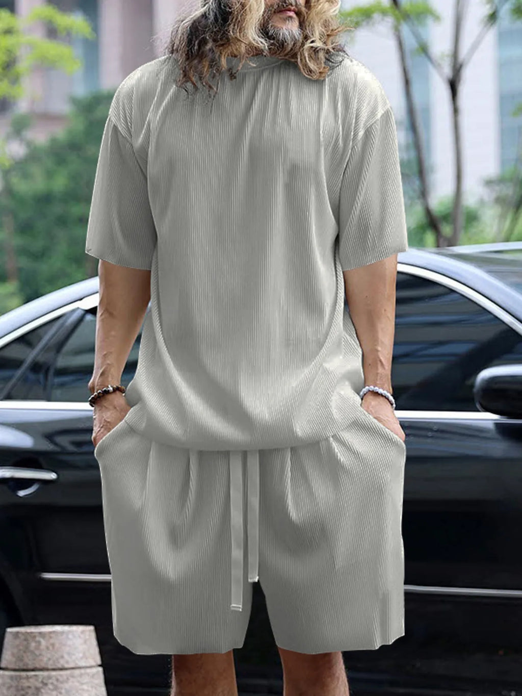 Person wearing a light gray outfit with a car and trees in the background