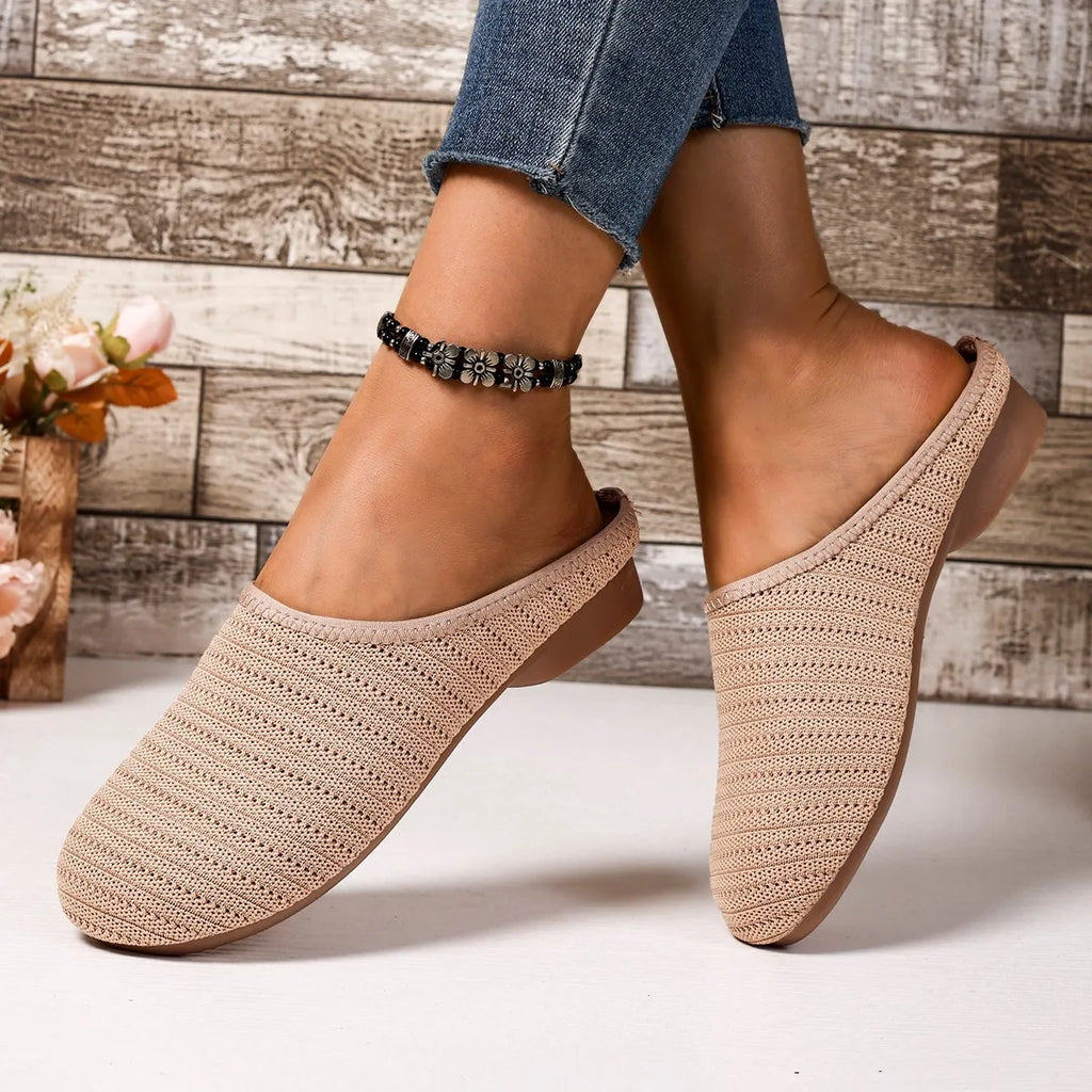 Beige crochet slippers worn with rolled-up jeans on a wooden floor background