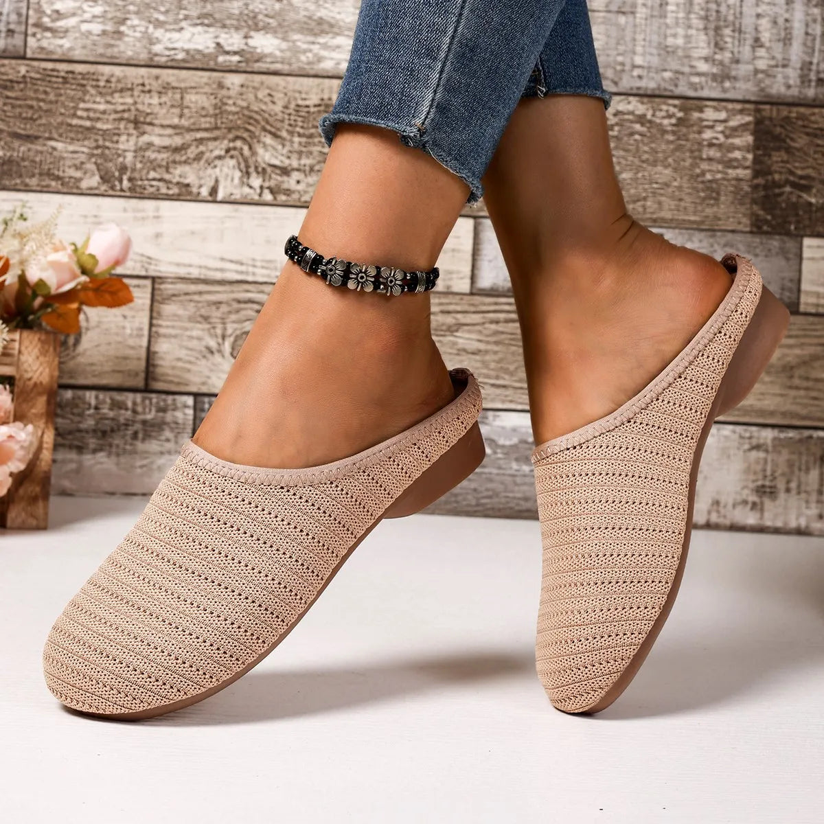 Beige crochet slippers worn with rolled-up jeans on a wooden floor background