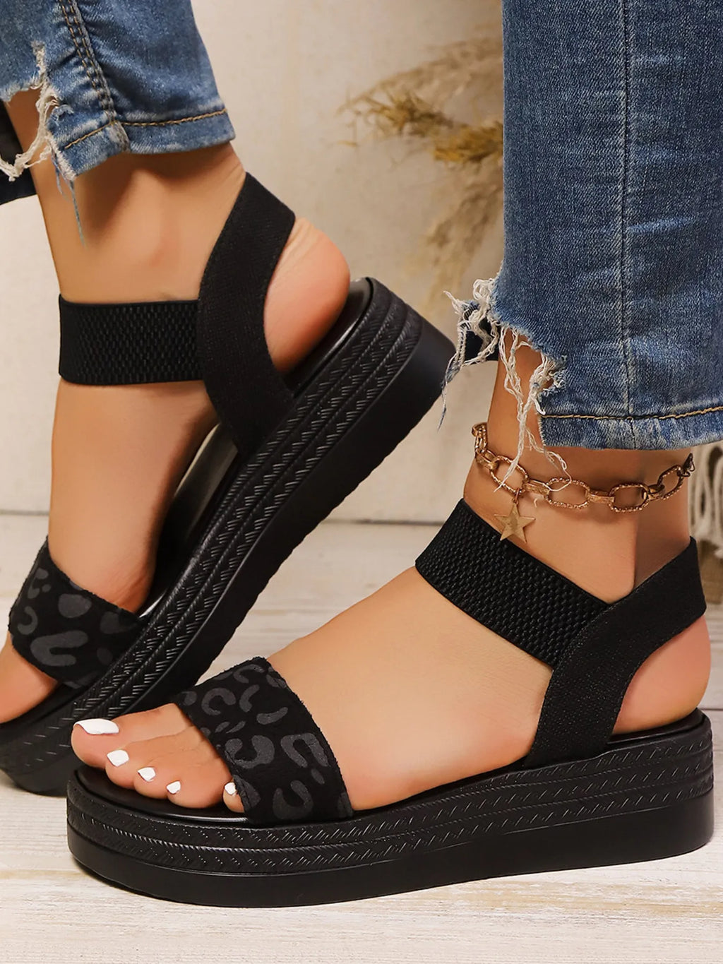 Black sandals with leopard print sole worn with ripped jeans on a light background