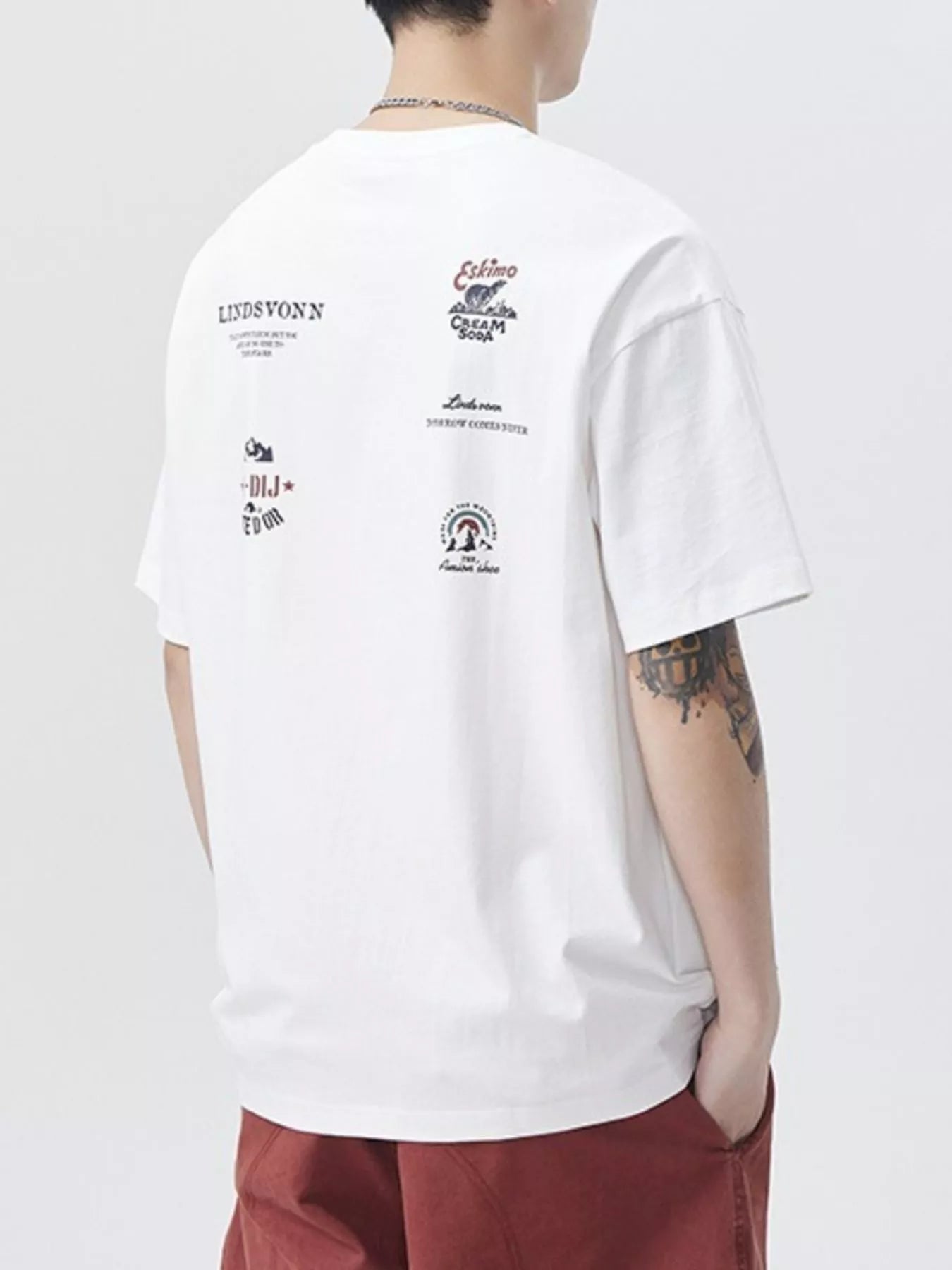 Person wearing a white t-shirt with multiple logos on the back, standing against a plain background-blackorvani.com