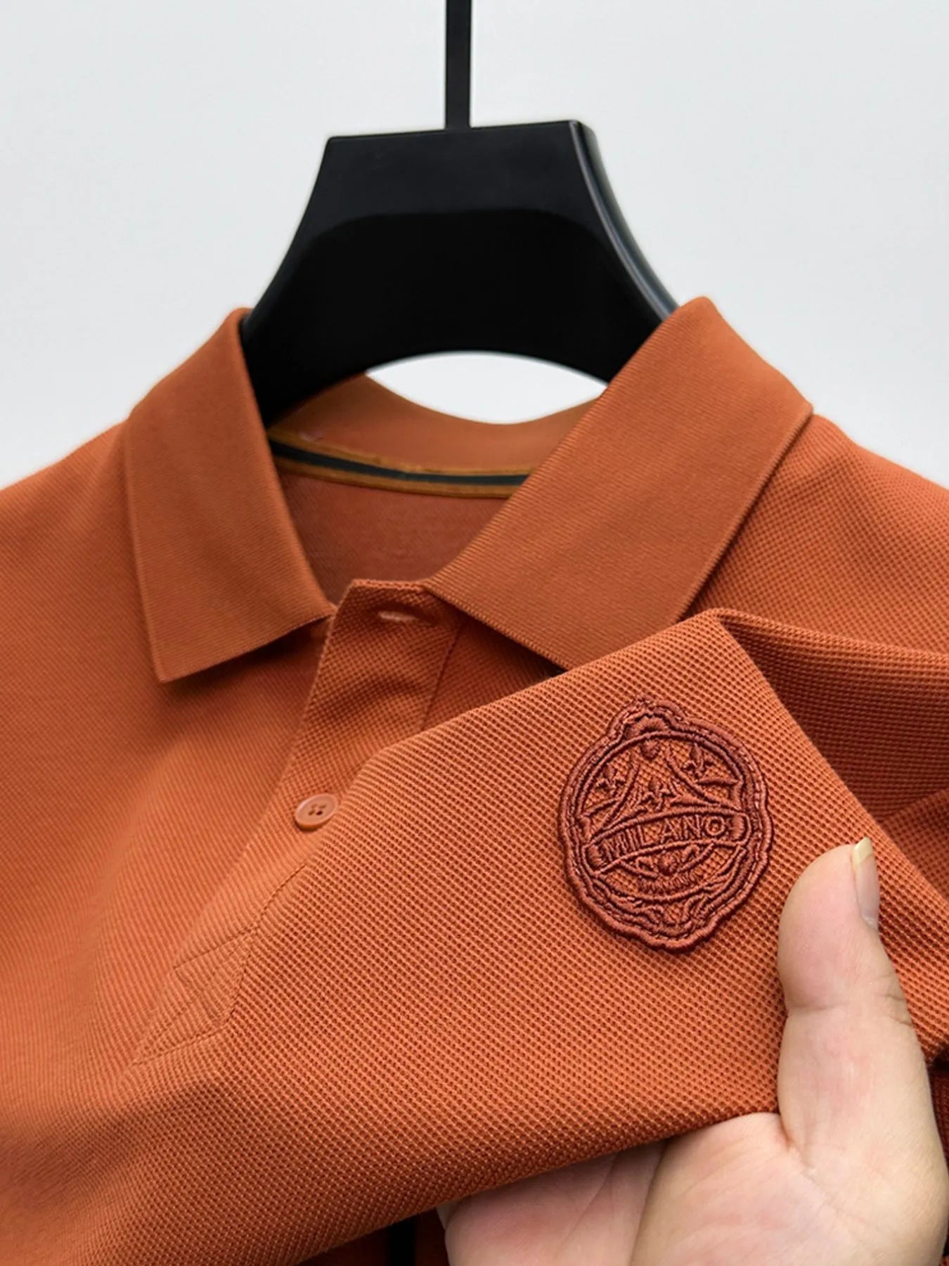 Brown polo shirt with a brand logo on a hanger against a white background