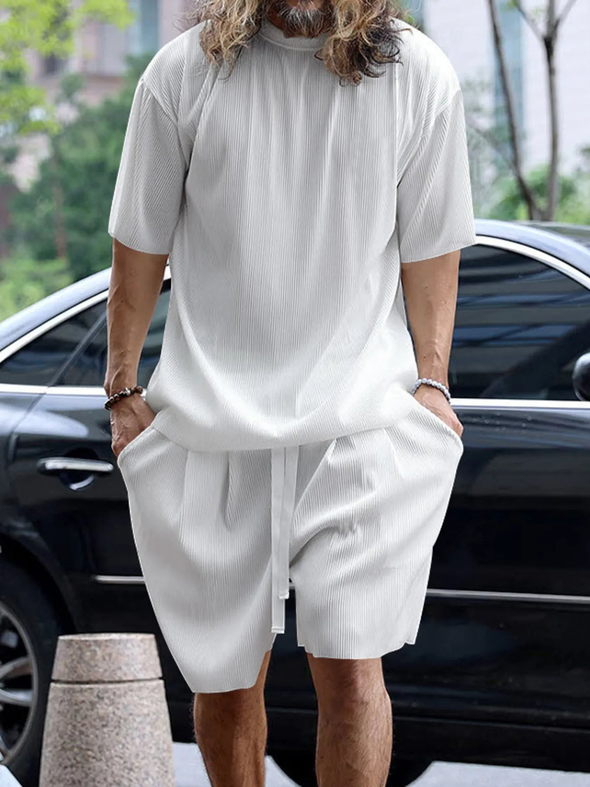 Person wearing a light gray outfit with a car and trees in the background