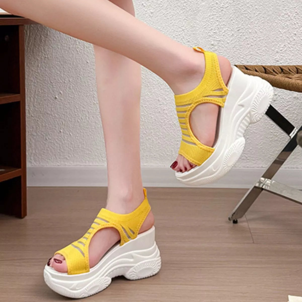 A person wearing bright yellow open-toe platform sandals with thick white soles, shown in a home interior setting with a textured wall and wood floor.
