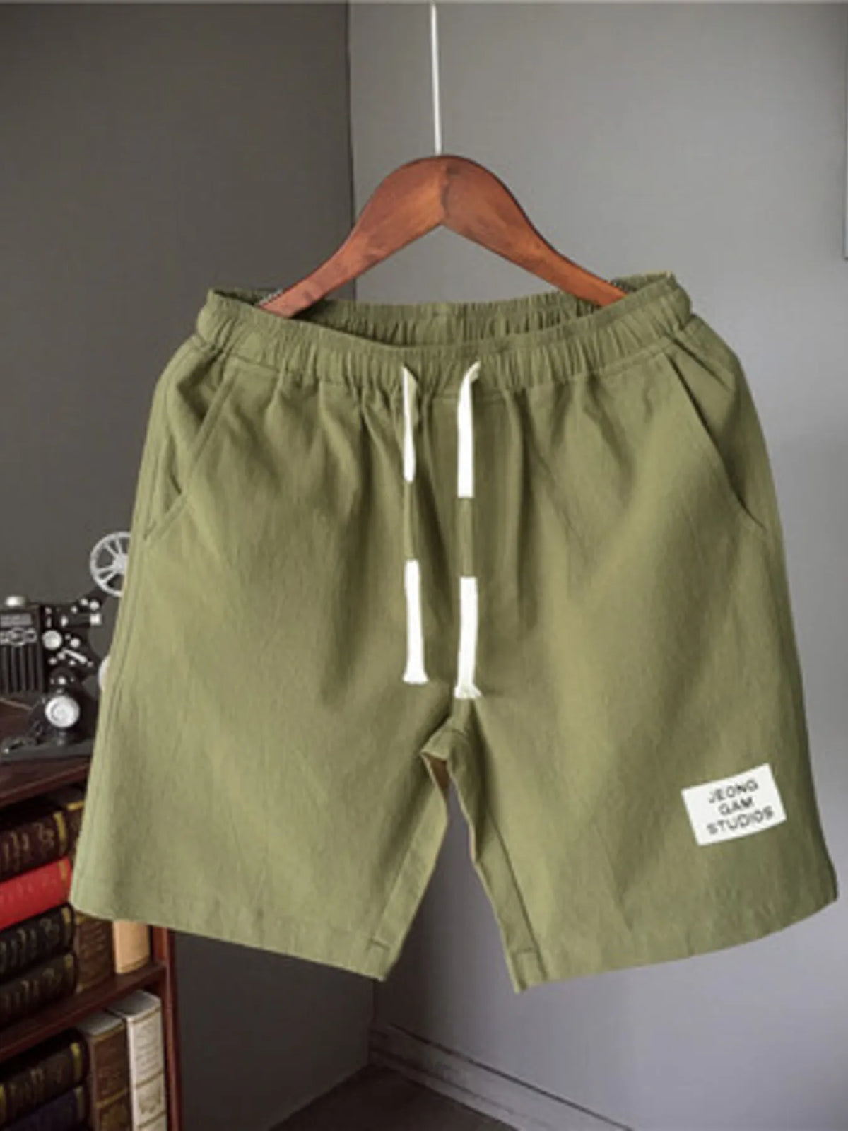 Green shorts with a label on a hanger against a gray wall.
