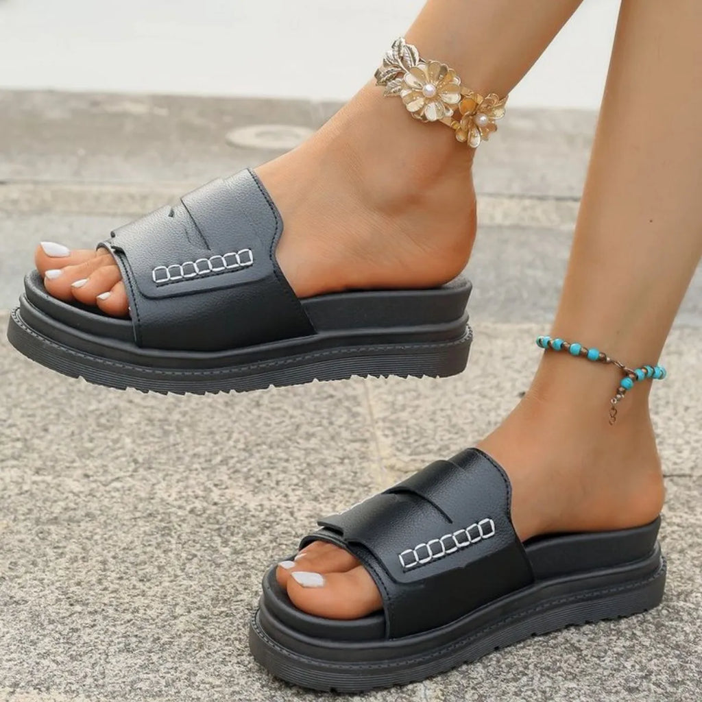 Black sandals worn on feet with a neutral background