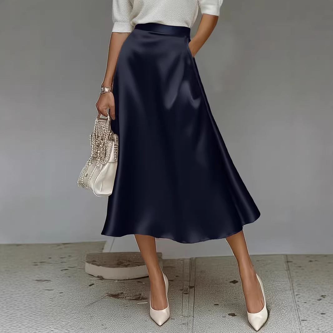 Person wearing a navy satin skirt with a white top and beige heels, holding a decorative handbag.
