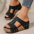 Black wedge sandals with cork platforms worn by a person on a neutral background
