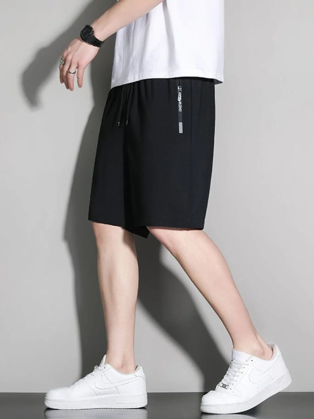 Person wearing black shorts and white sneakers on a plain background