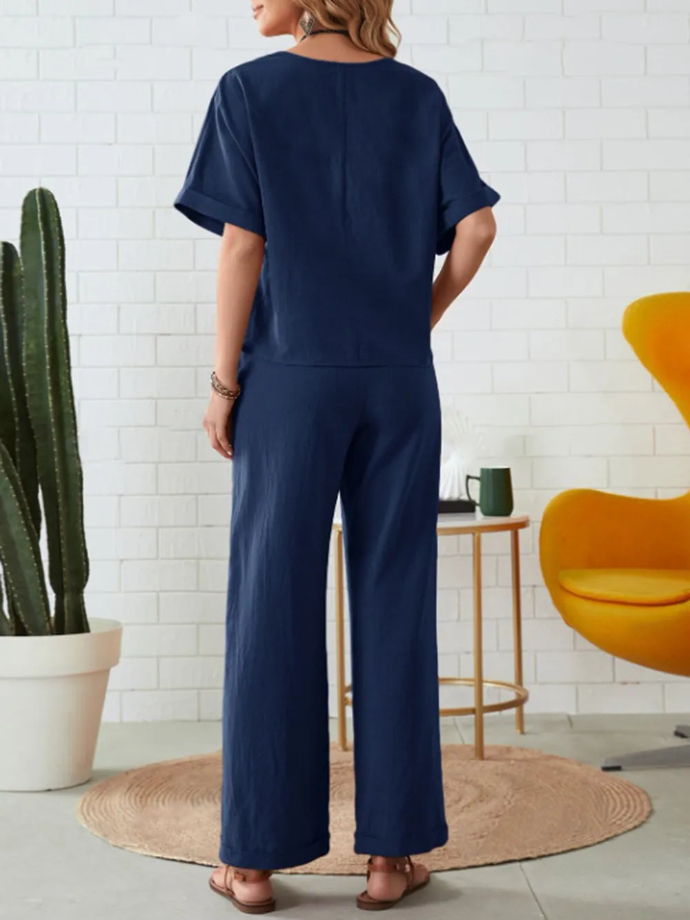 Person wearing a navy blue outfit standing in a room with a white tiled wall, yellow chair, and potted plant-blackorvani