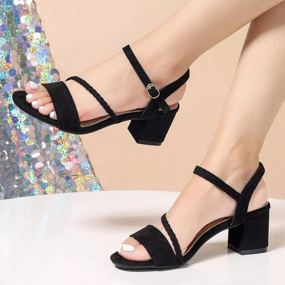 Black strappy block-heel sandals worn on a model's feet, shown against a neutral beige background with a colorful sequined fabric prop-blackorvani.com