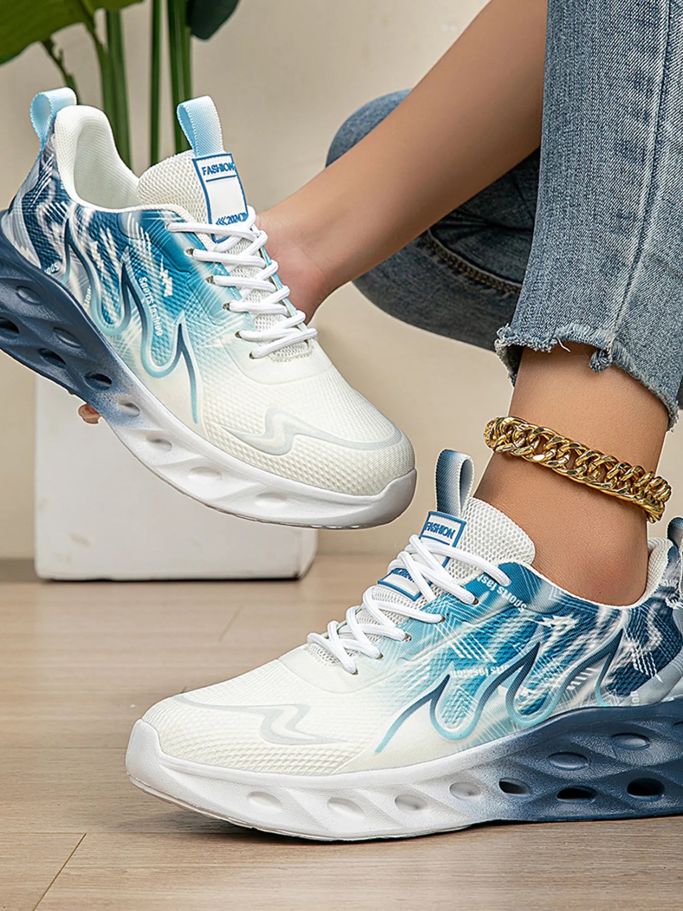 White and blue sneakers with a gradient design worn by a person on a light wooden floor.