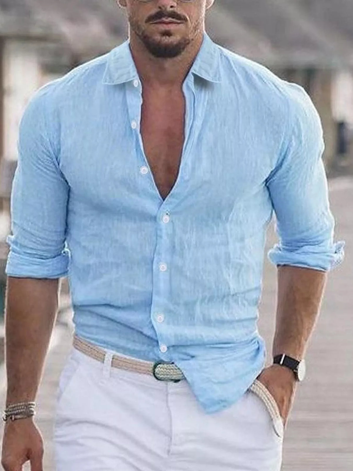 Man wearing a light blue button-up shirt with rolled-up sleeves and white pants.