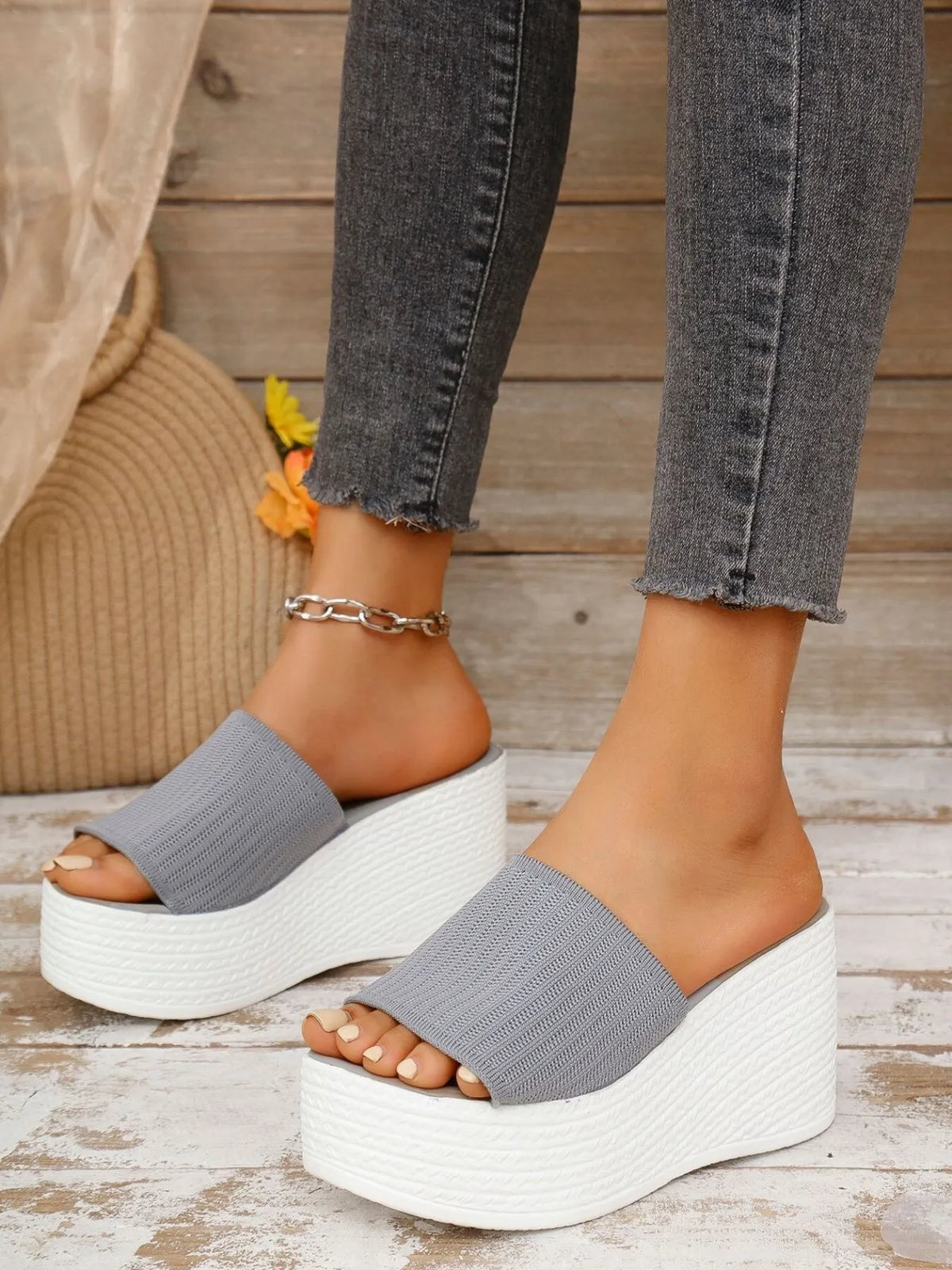 Gray platform sandals worn with gray jeans on a wooden floor.