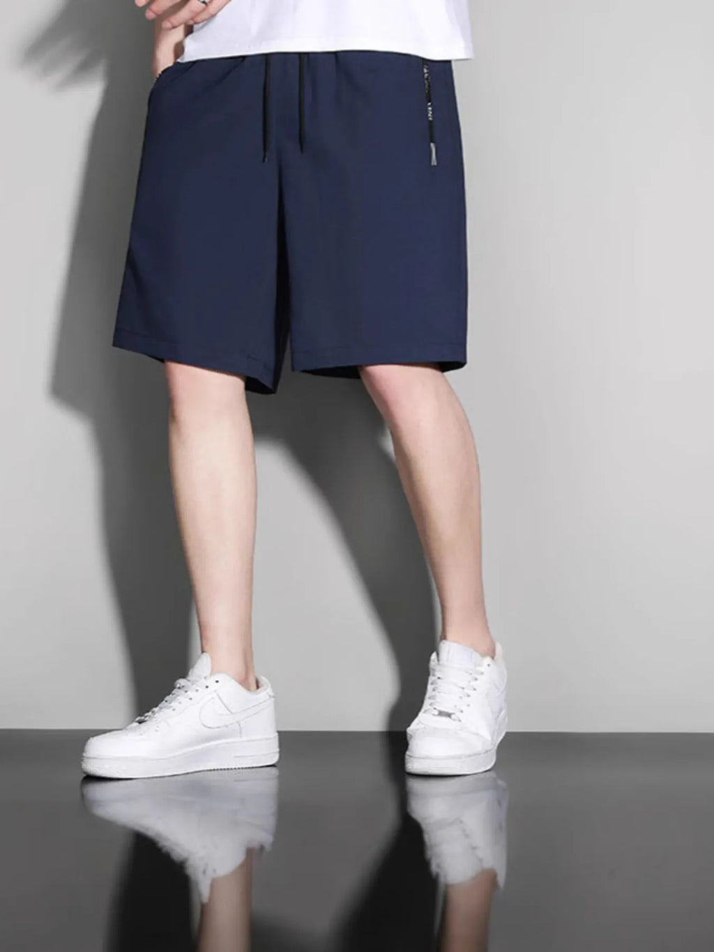Person wearing navy shorts and white sneakers on a gray background