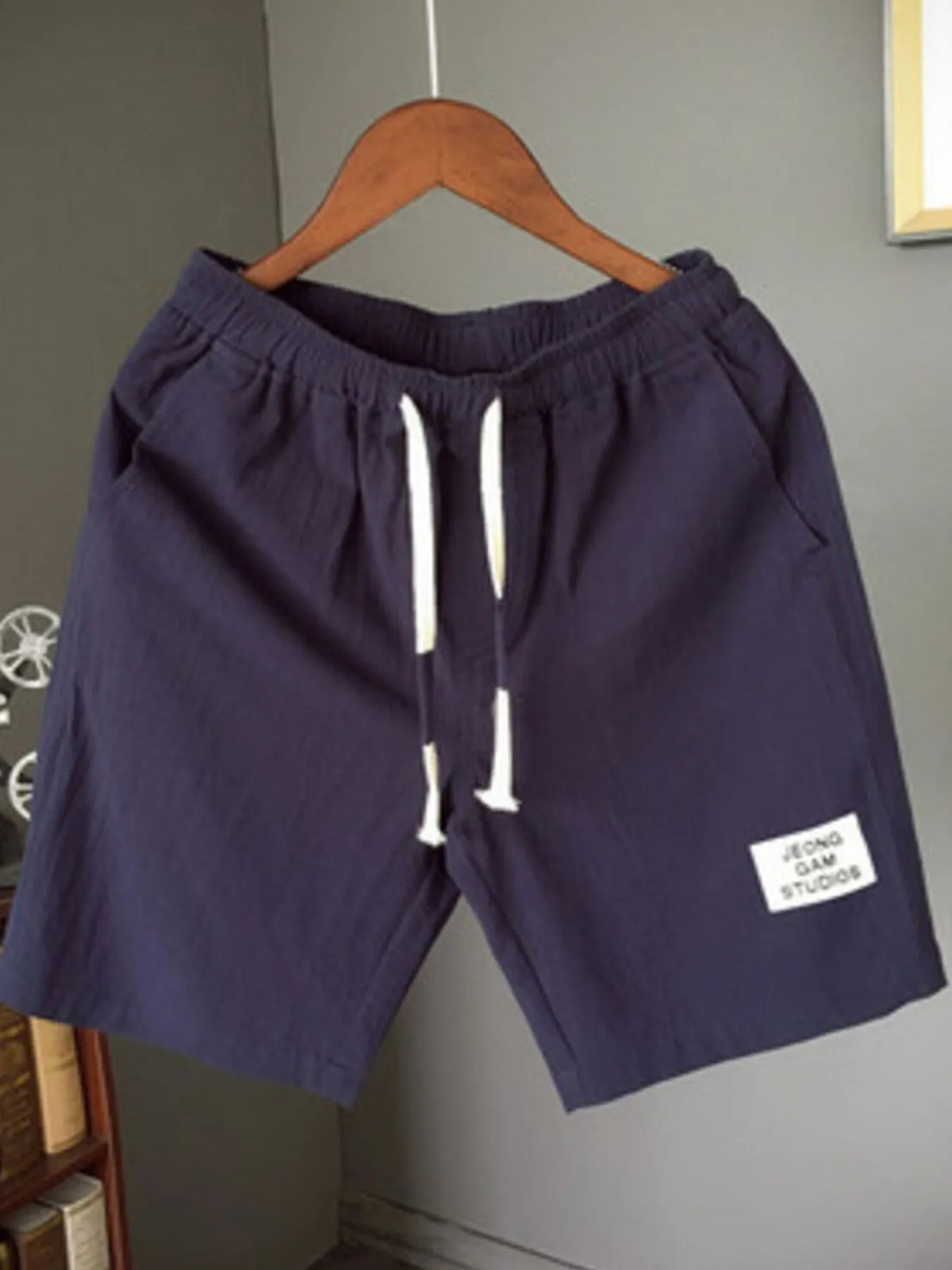 Navy blue shorts with a white label on a hanger against a gray wall.