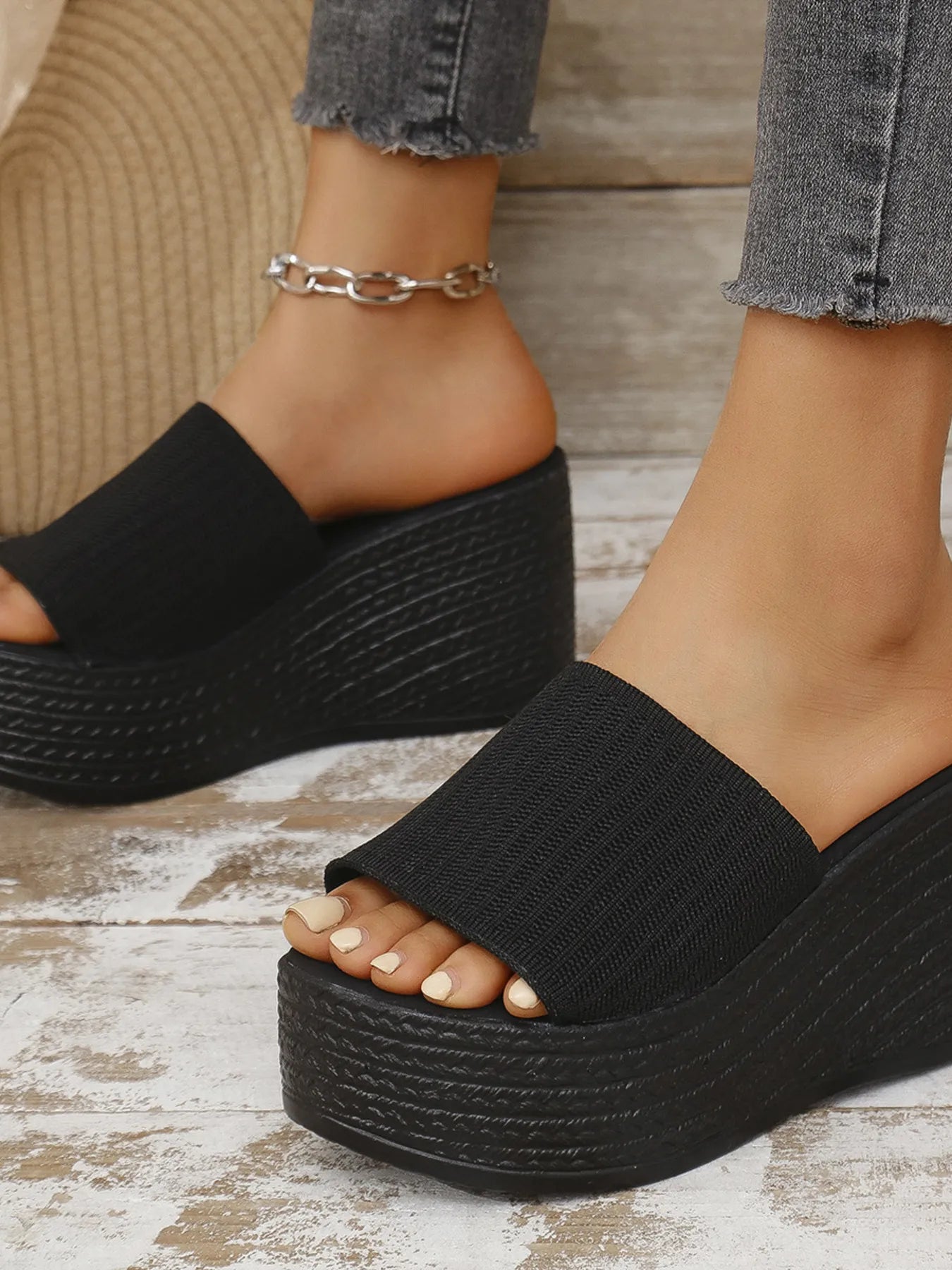 Black wedge sandals worn on a wooden floor