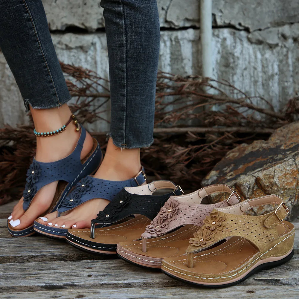 Pair of sandals displayed on a wooden surface with a stone wall background