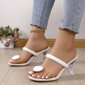 White high-heeled sandals worn with light blue jeans on a wooden floor.