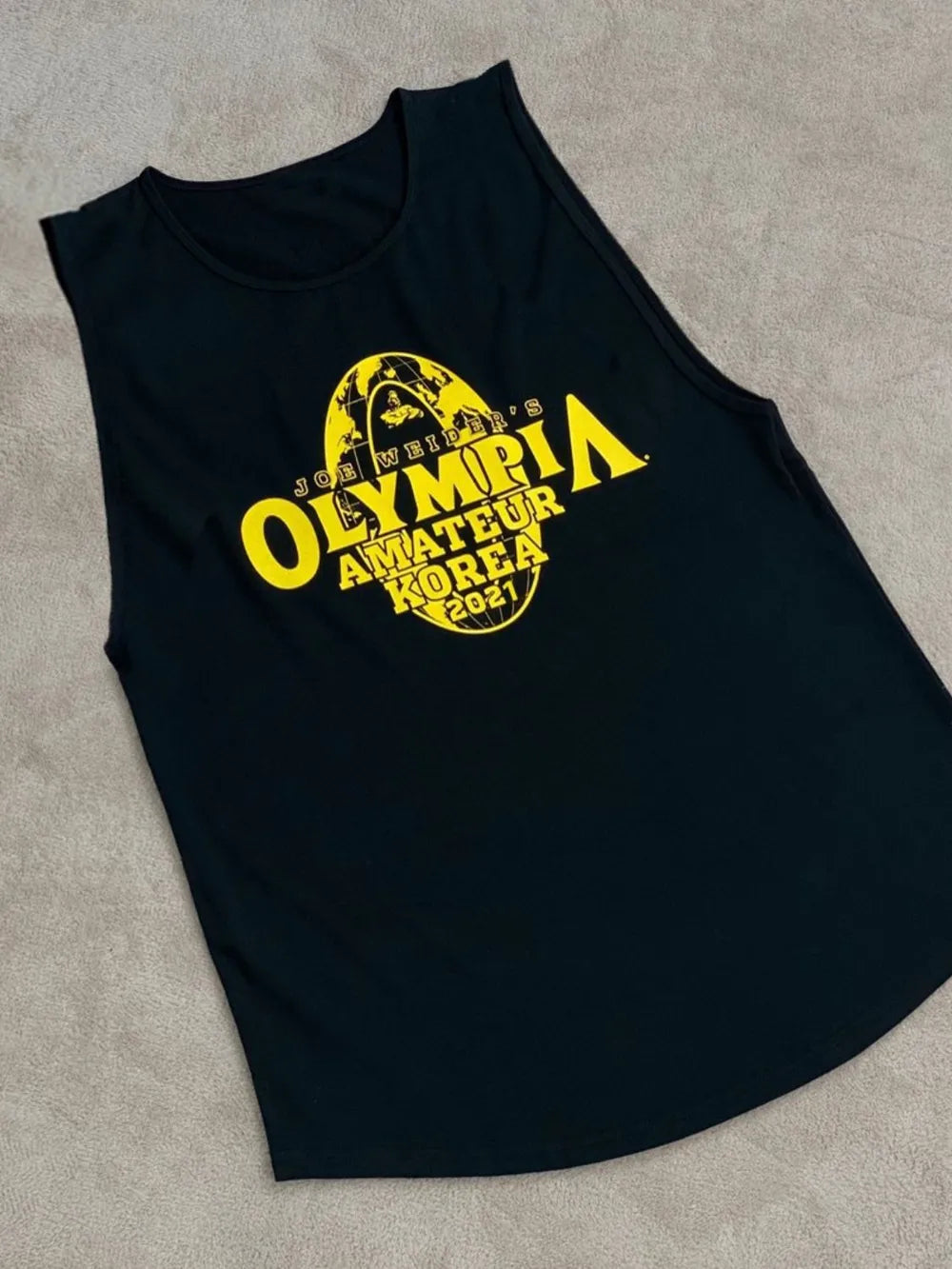 Black sleeveless shirt with yellow 'Olympia Amateur' logo on a gray surface-blackorvani.com