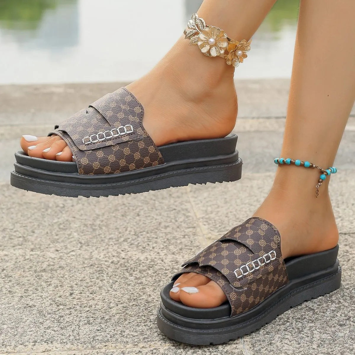 Brown patterned sandals with black soles worn by a person on a concrete surface.