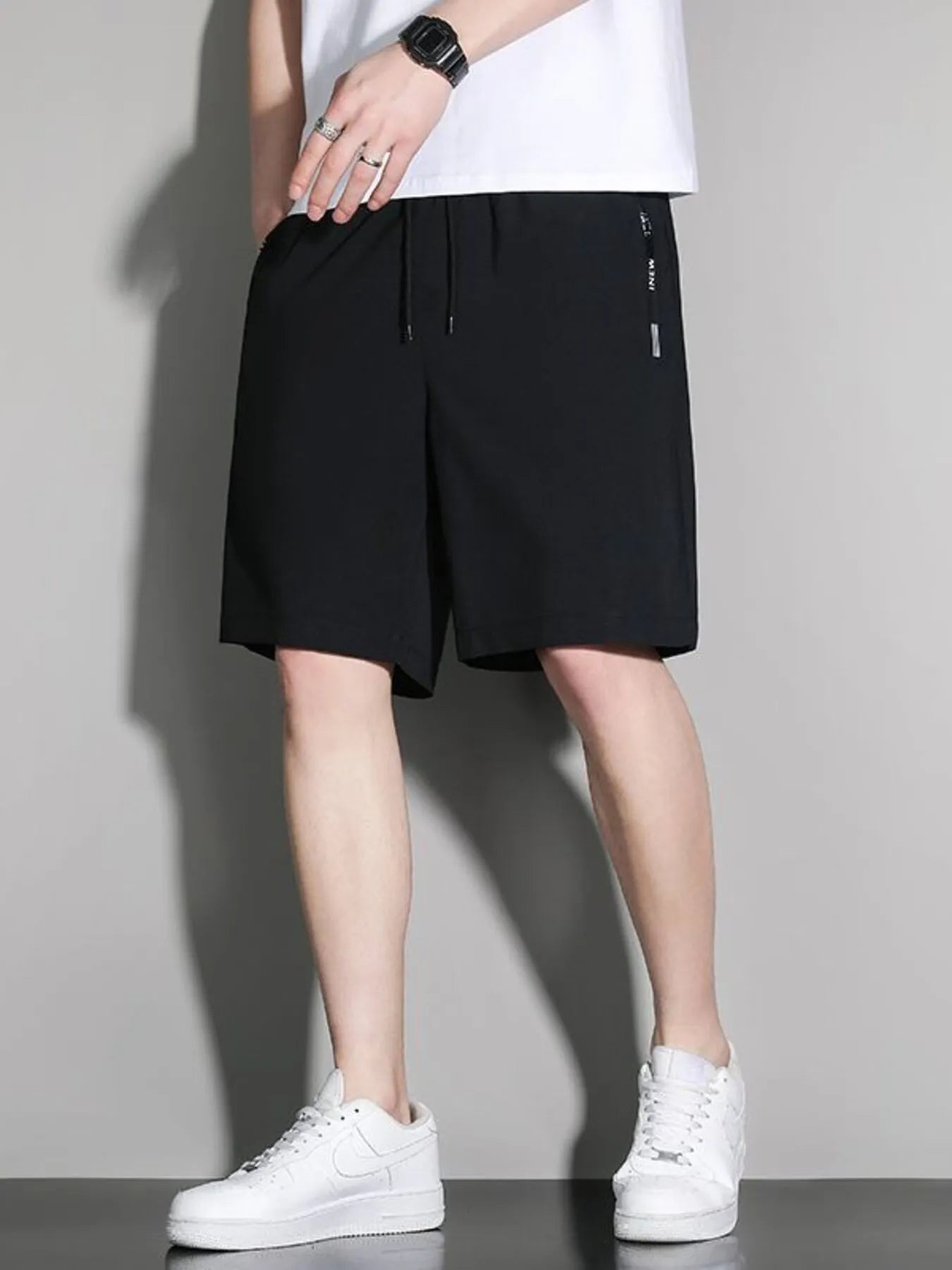 Person wearing black shorts and white sneakers on a gray background